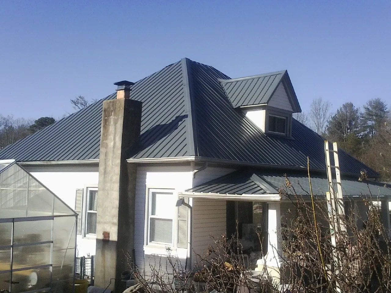 Dark blue standing seam metal roof on a white farmhouse with dormer — Slate & Tile Roof Repair by Roofing Brothers in Iola