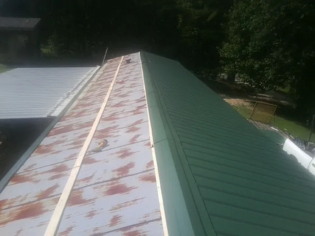 Old rusted panels beside newly installed green metal roofing — Wind Damage Roof Repair by Roofing Brothers in Iola