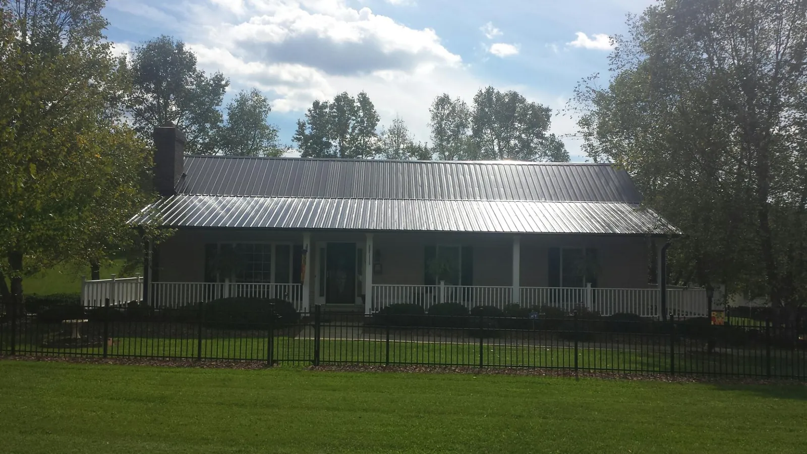 Gray metal roof on a brick ranch with a full width front porch — Gutter Guard Installation work by our crew in Iola