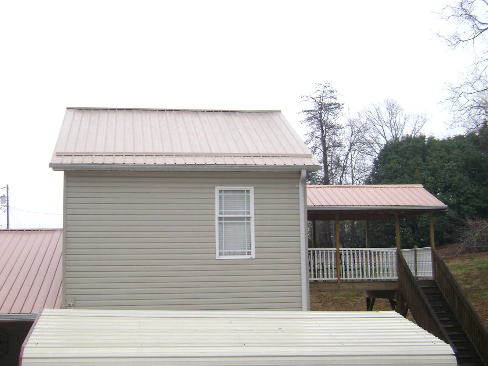 Tan metal roofs on a two story addition and attached porch, from a Roof Replacement job in Iola